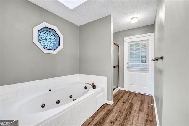 bathroom with a textured ceiling, hardwood / wood-style flooring, a skylight, and shower with separate bathtub