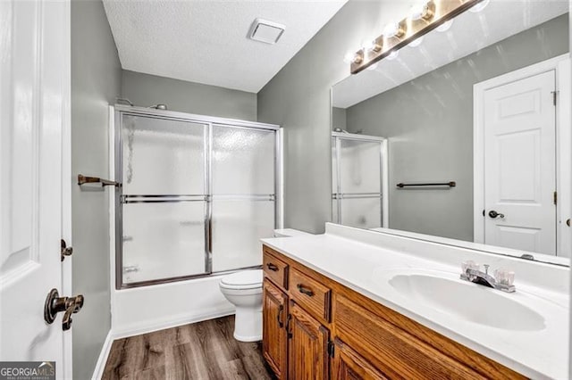 full bathroom featuring vanity, enclosed tub / shower combo, hardwood / wood-style flooring, toilet, and a textured ceiling