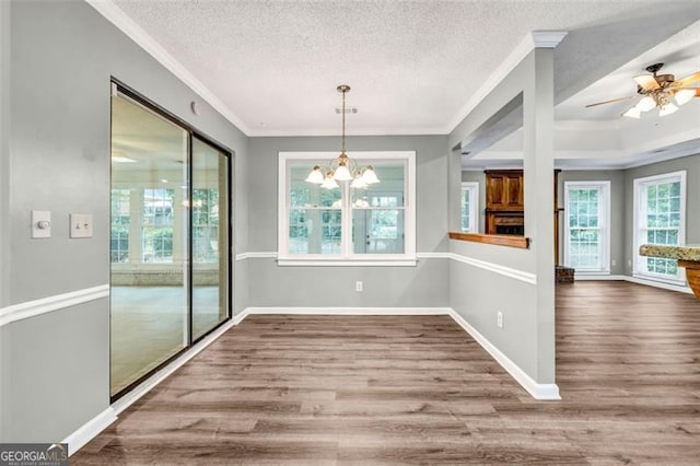 unfurnished dining area with hardwood / wood-style flooring, ceiling fan with notable chandelier, ornamental molding, and a textured ceiling