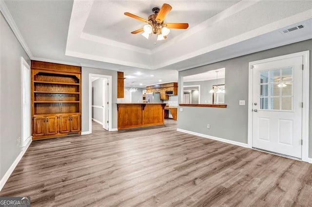 unfurnished living room featuring ceiling fan with notable chandelier, light wood-type flooring, crown molding, and a tray ceiling