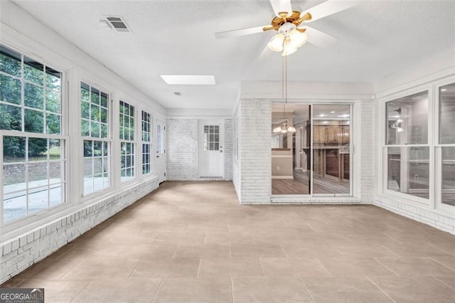 unfurnished sunroom featuring ceiling fan with notable chandelier and a skylight