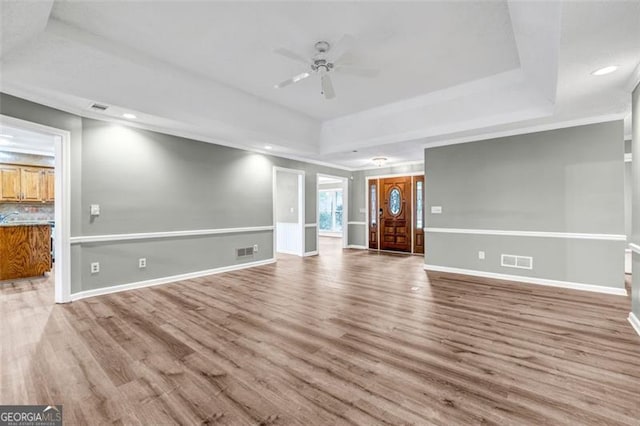 unfurnished living room featuring a tray ceiling, hardwood / wood-style flooring, and ceiling fan