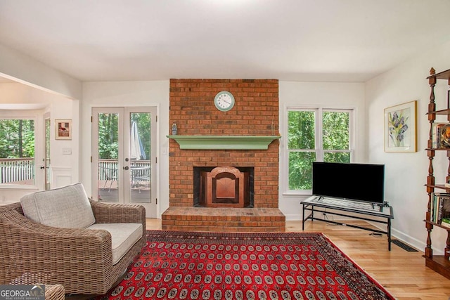 living room with hardwood / wood-style flooring, a healthy amount of sunlight, a brick fireplace, and french doors