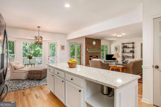 kitchen with a healthy amount of sunlight, pendant lighting, a kitchen island, light hardwood / wood-style flooring, and white cabinets