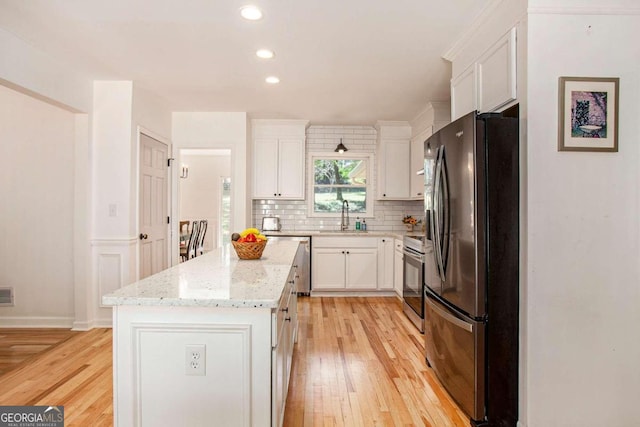 kitchen featuring a kitchen island, light stone counters, light wood-type flooring, stainless steel appliances, and white cabinets