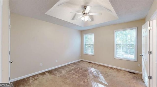 carpeted empty room with a raised ceiling and ceiling fan