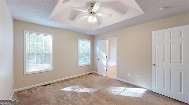 unfurnished bedroom with multiple windows, ceiling fan, a tray ceiling, and light colored carpet