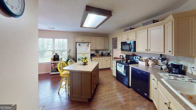 kitchen with cream cabinetry, black appliances, a kitchen island, and dark hardwood / wood-style flooring