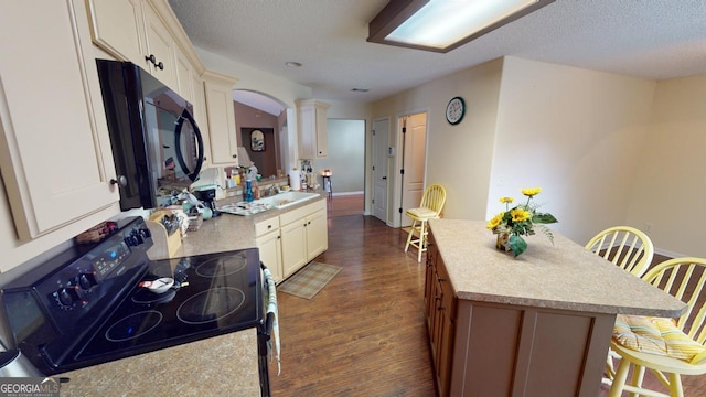 kitchen with ornate columns, a textured ceiling, dark hardwood / wood-style flooring, and black appliances