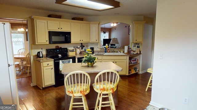 kitchen featuring a breakfast bar area, black appliances, dark hardwood / wood-style flooring, and cream cabinetry