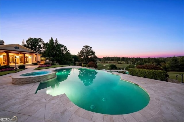 pool at dusk with an in ground hot tub and a patio