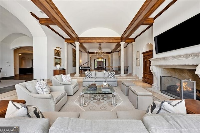 living room with a premium fireplace, beamed ceiling, ornate columns, and an inviting chandelier