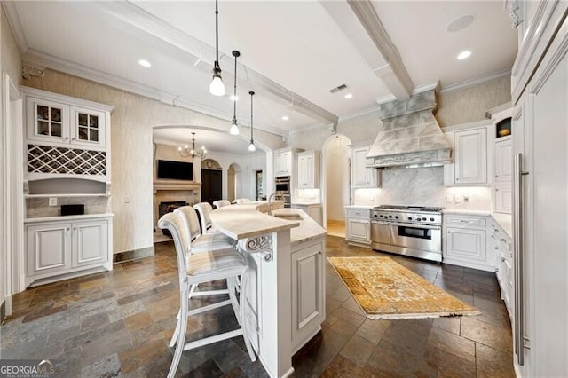 kitchen featuring a kitchen island with sink, white cabinets, pendant lighting, custom exhaust hood, and appliances with stainless steel finishes