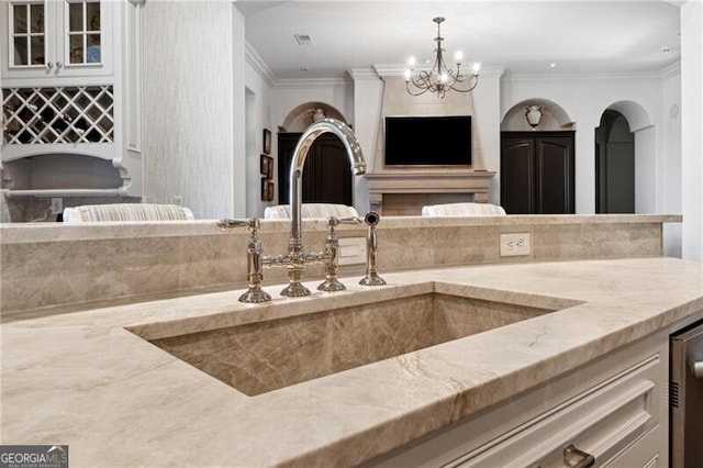 kitchen featuring sink, decorative light fixtures, a chandelier, light stone countertops, and crown molding