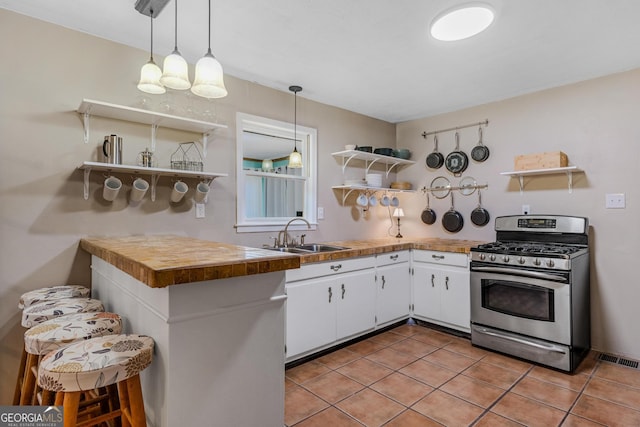 kitchen featuring white cabinets, stainless steel gas stove, sink, kitchen peninsula, and decorative light fixtures