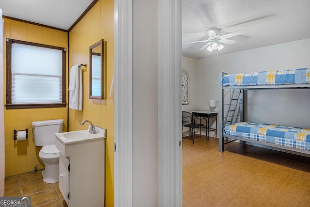 bathroom featuring ceiling fan, vanity, a textured ceiling, wooden walls, and toilet