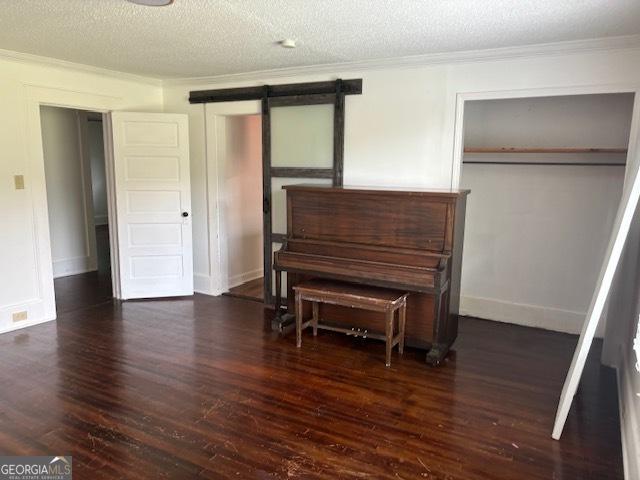 miscellaneous room with crown molding, a barn door, dark hardwood / wood-style flooring, and a textured ceiling