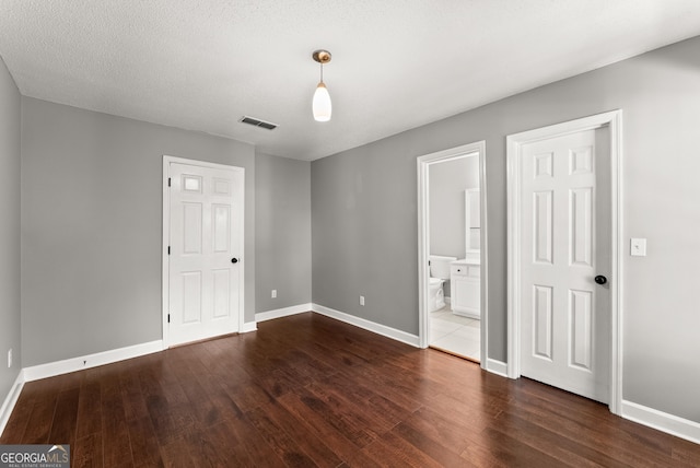 unfurnished bedroom with ensuite bathroom, dark wood-type flooring, and a textured ceiling