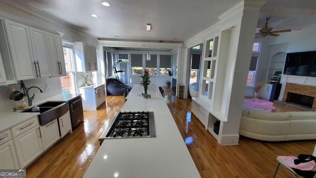 kitchen featuring gas cooktop, ornamental molding, sink, light wood-type flooring, and white cabinets