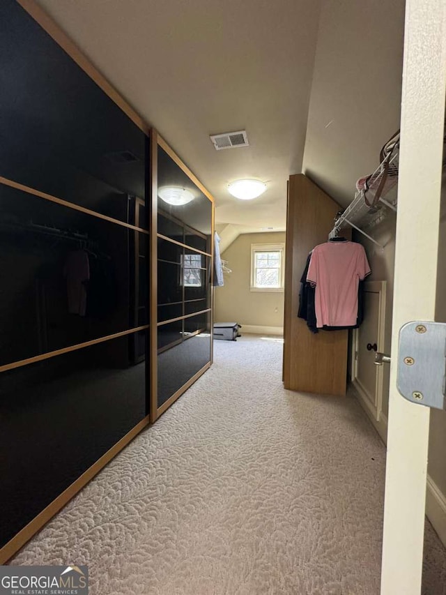 spacious closet with vaulted ceiling, carpet flooring, and visible vents