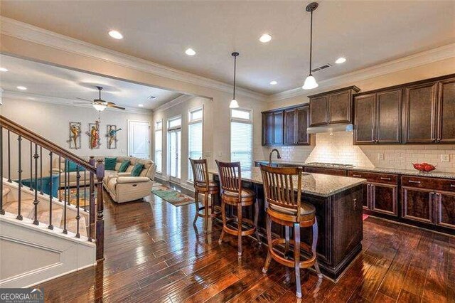 kitchen with dark brown cabinets, light stone countertops, a kitchen island with sink, and dark hardwood / wood-style flooring