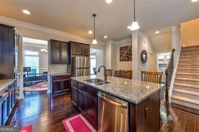 kitchen featuring stainless steel appliances, dark wood-type flooring, sink, pendant lighting, and a center island with sink