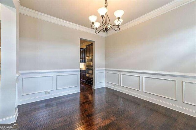 empty room with dark hardwood / wood-style floors, an inviting chandelier, and ornamental molding