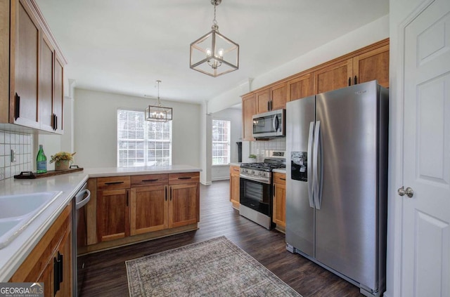 kitchen featuring kitchen peninsula, tasteful backsplash, decorative light fixtures, appliances with stainless steel finishes, and dark hardwood / wood-style floors