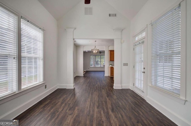 interior space with dark wood-type flooring, plenty of natural light, ceiling fan with notable chandelier, and decorative columns