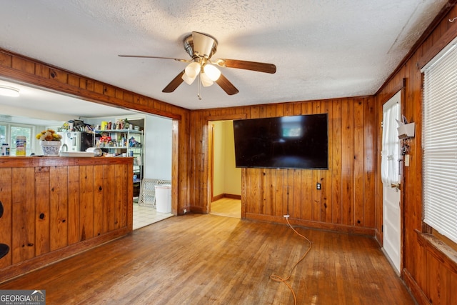 unfurnished living room featuring a textured ceiling, wood walls, hardwood / wood-style floors, and plenty of natural light