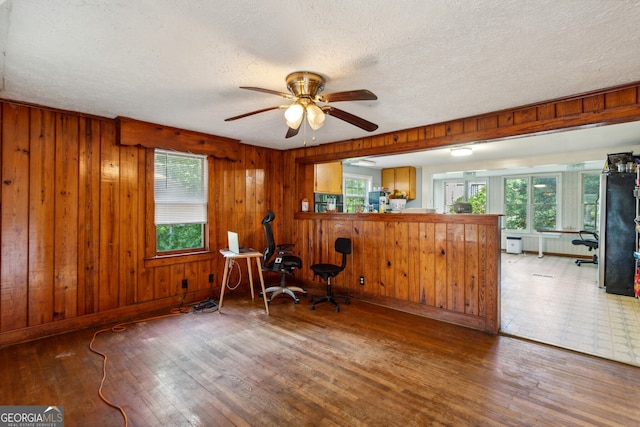 unfurnished room with hardwood / wood-style flooring, ceiling fan, wooden walls, and a wealth of natural light