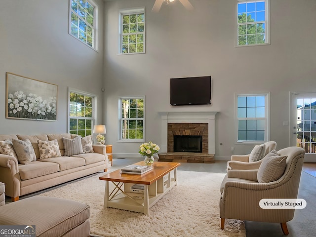 living room with a high ceiling, a healthy amount of sunlight, ceiling fan, and a stone fireplace