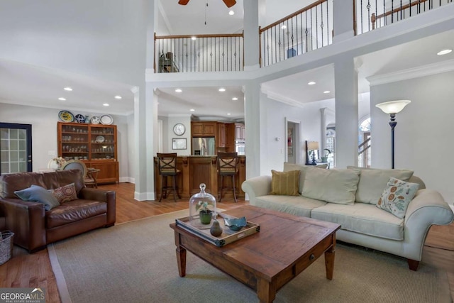 living room with ceiling fan, ornamental molding, decorative columns, a high ceiling, and light wood-type flooring