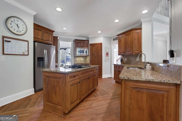 kitchen featuring light wood-type flooring, sink, light stone counters, appliances with stainless steel finishes, and a center island