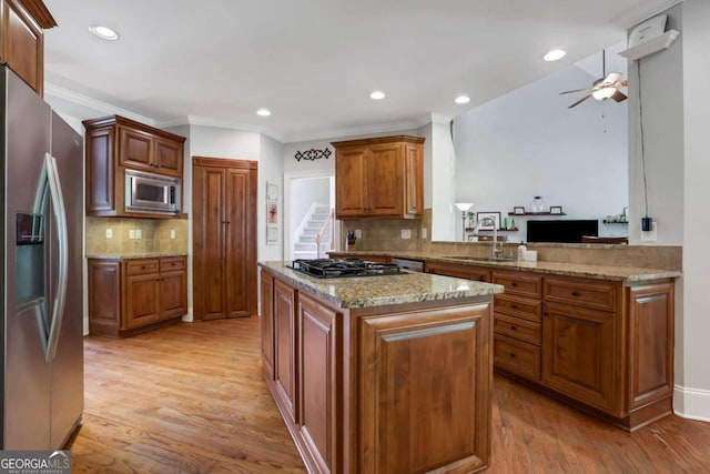 kitchen featuring light wood-type flooring, sink, light stone countertops, appliances with stainless steel finishes, and a center island