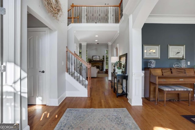 foyer with ornamental molding, hardwood / wood-style flooring, decorative columns, and a high ceiling