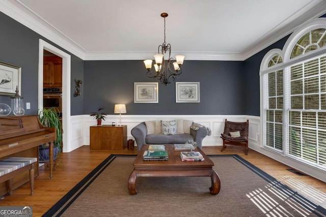 living room with a notable chandelier, plenty of natural light, ornamental molding, and hardwood / wood-style flooring