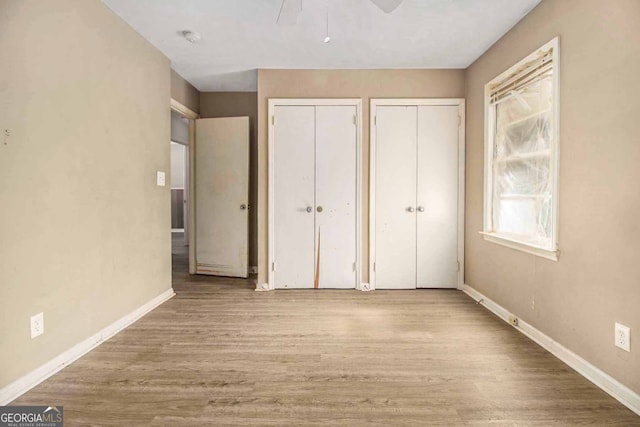 unfurnished bedroom featuring light hardwood / wood-style floors, two closets, and ceiling fan