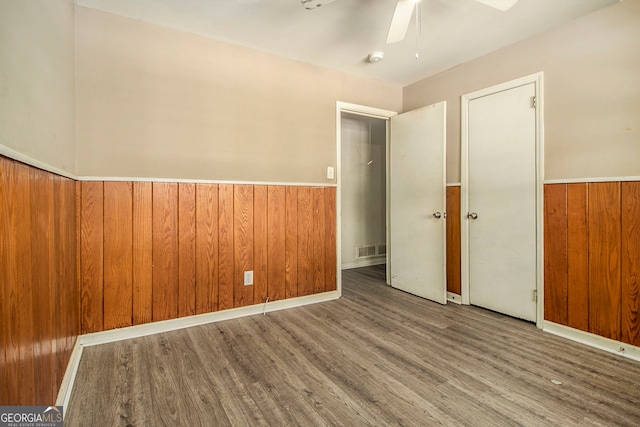 unfurnished bedroom with ceiling fan, wood walls, and hardwood / wood-style floors