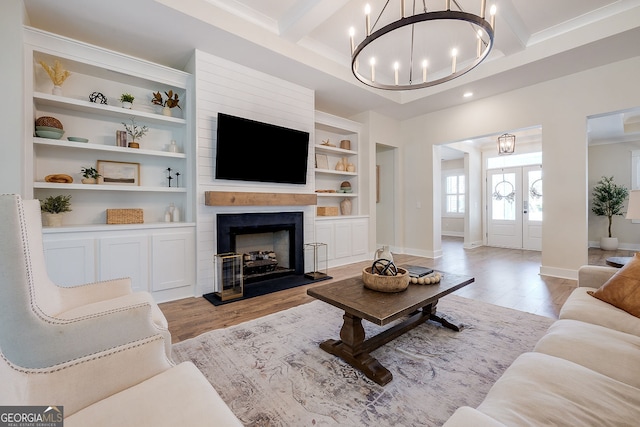 living room featuring light hardwood / wood-style floors, a notable chandelier, beamed ceiling, and a fireplace