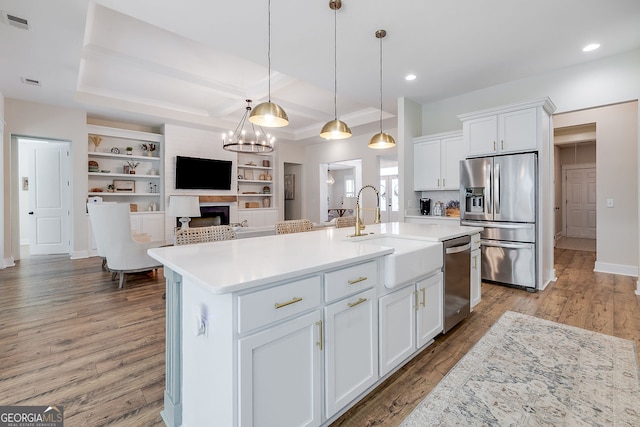 kitchen with a kitchen island with sink, dark wood-type flooring, stainless steel appliances, sink, and white cabinetry