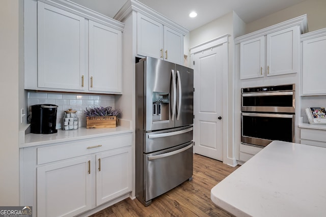 kitchen featuring appliances with stainless steel finishes, white cabinets, hardwood / wood-style flooring, and backsplash