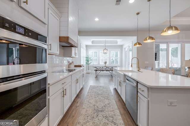 kitchen with wood-type flooring, a center island with sink, a wealth of natural light, decorative light fixtures, and appliances with stainless steel finishes