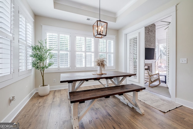 dining room featuring a notable chandelier, a tray ceiling, and light wood-type flooring