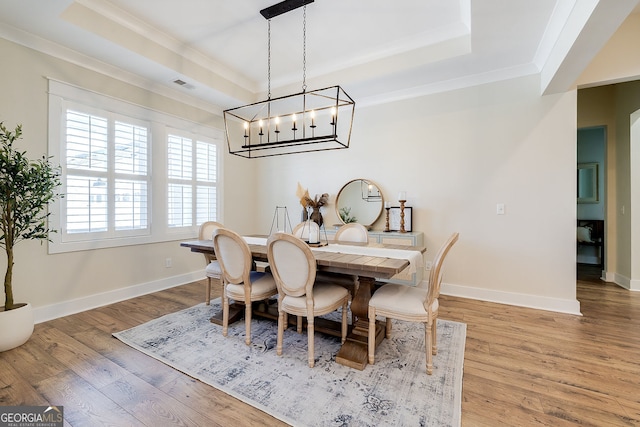 dining area featuring a raised ceiling, ornamental molding, an inviting chandelier, and hardwood / wood-style floors