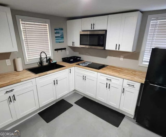 kitchen featuring white cabinets, sink, black refrigerator, and wood counters