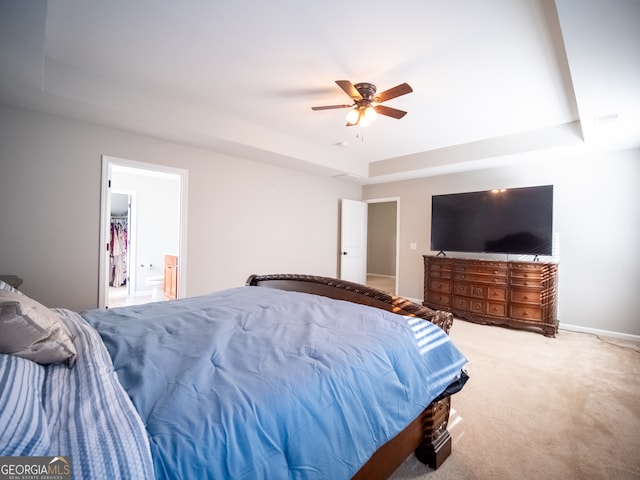 carpeted bedroom with a tray ceiling, connected bathroom, and ceiling fan