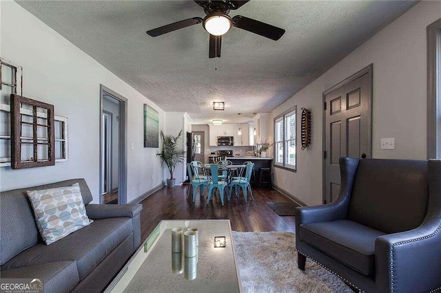 living room with ceiling fan, a textured ceiling, and dark wood-type flooring