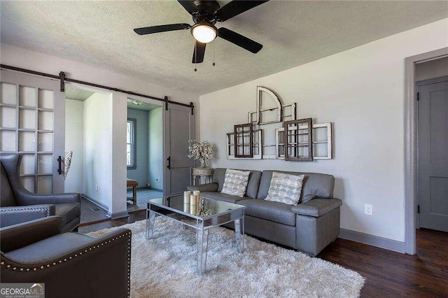 living room with a barn door, ceiling fan, hardwood / wood-style floors, and a textured ceiling