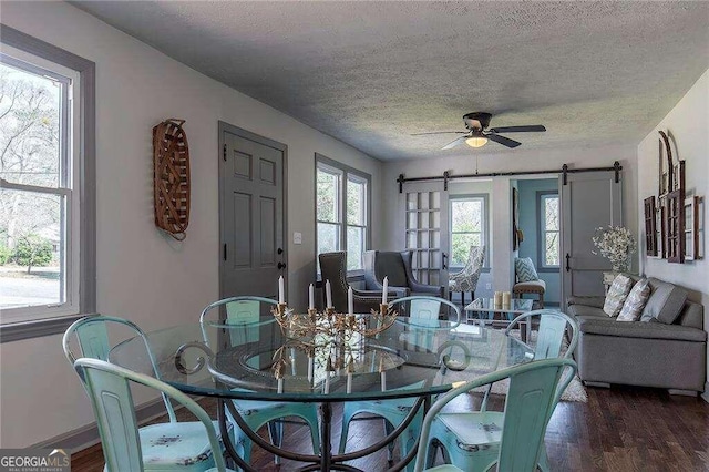 dining room featuring a barn door, dark hardwood / wood-style flooring, a textured ceiling, and ceiling fan